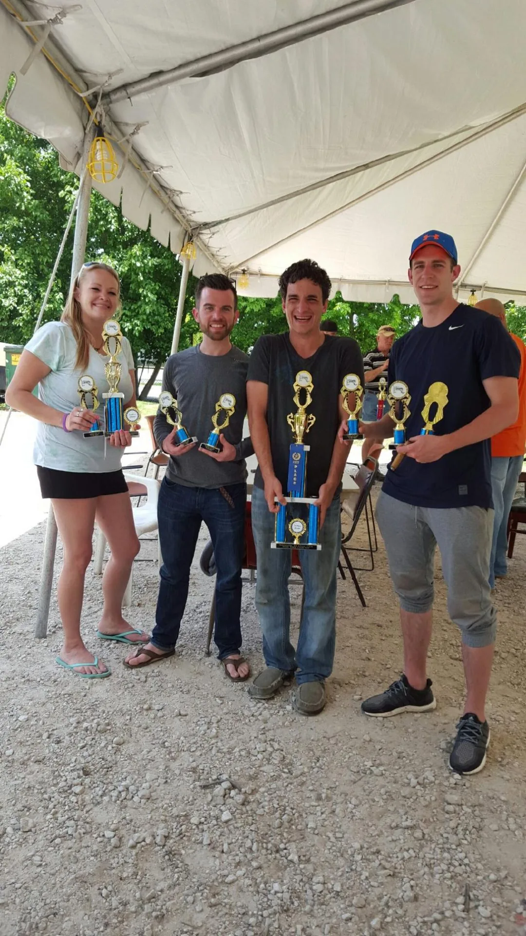 A group of four young adults standing under a canopy, proudly holding trophies together after a group activity during recovery.
