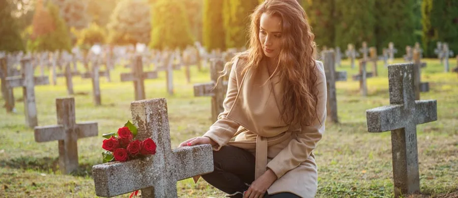 woman sitting by a tombstone at a cemetery
