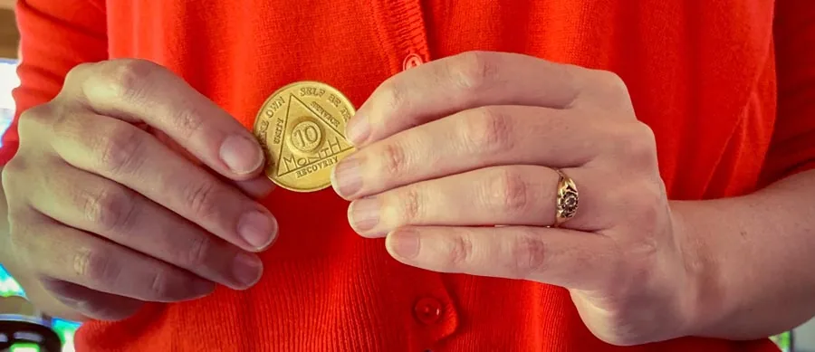 Hands holding a bronze 10-month AA medallion stamped with the AA triangle