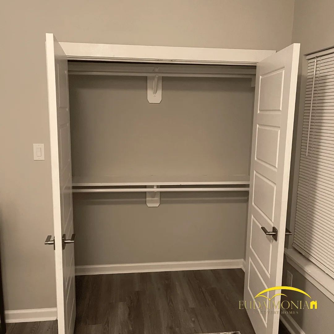 Bedroom closet with a hanging rail and shelf behind white bifold doors.