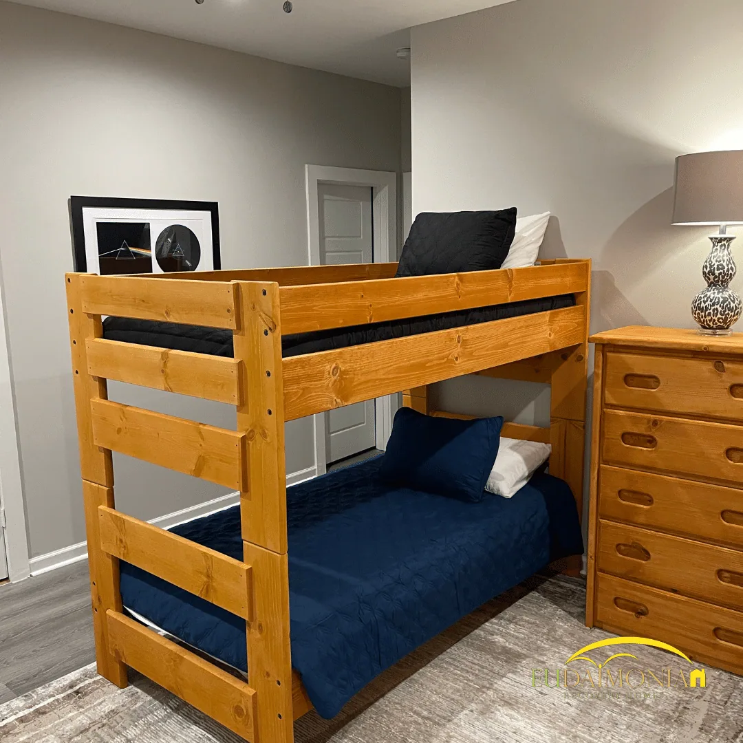 Pine bunk bed with navy bedding beside a wooden dresser and table lamp.