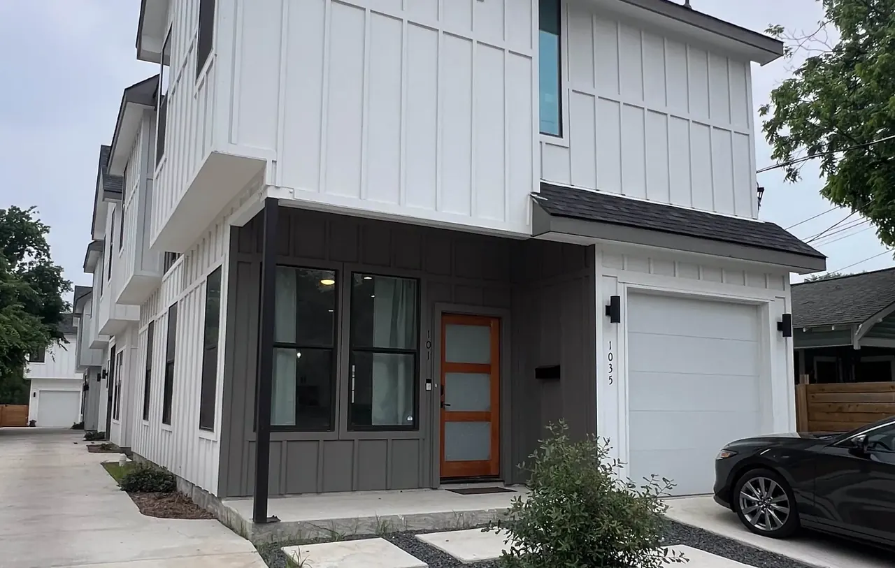 Front elevation of the San Antonio house: two-story, white board-and-batten over a dark lower level, with a wood front door and an attached garage.