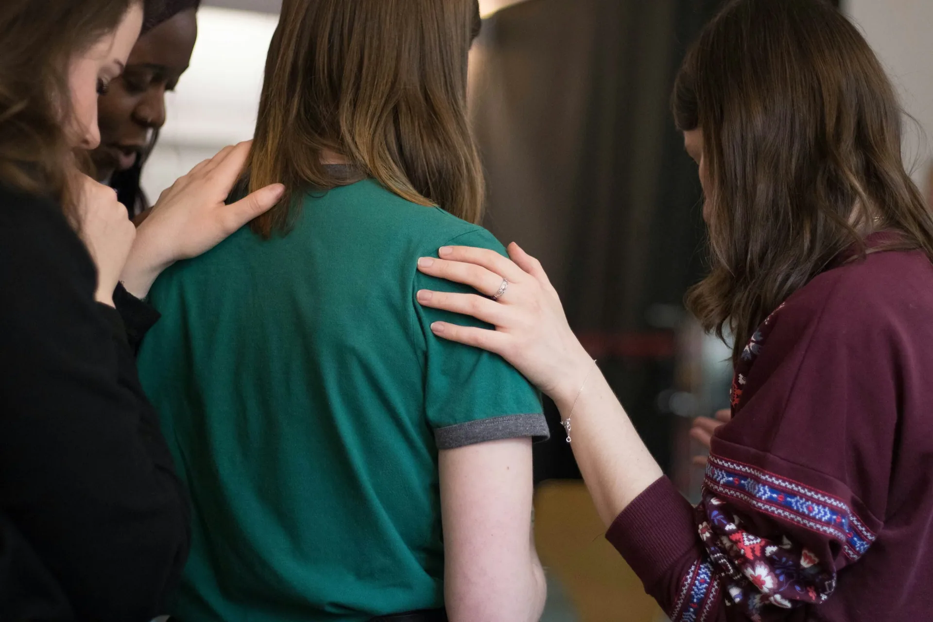 Group of people placing hands on one person’s shoulder, symbolizing community support in sobriety.