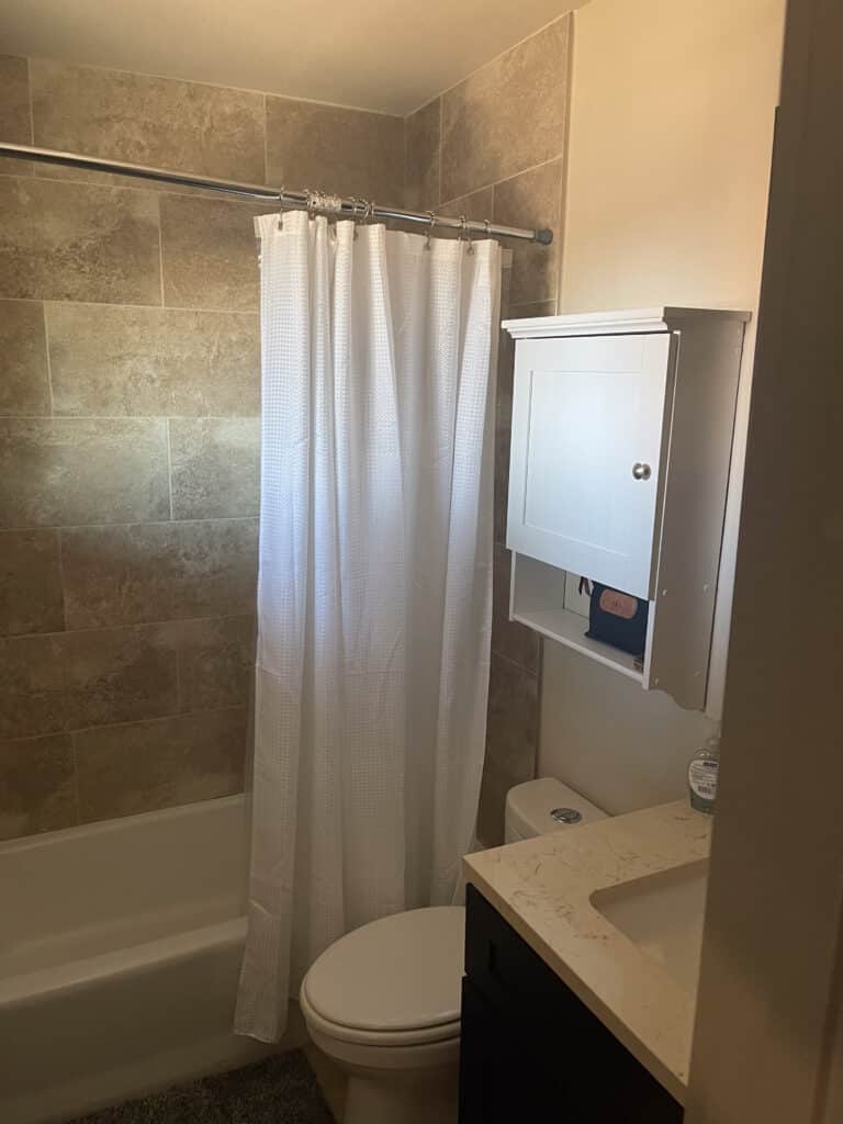 Clean bathroom in Austin sober living home with tiled shower, white curtain, and modern vanity