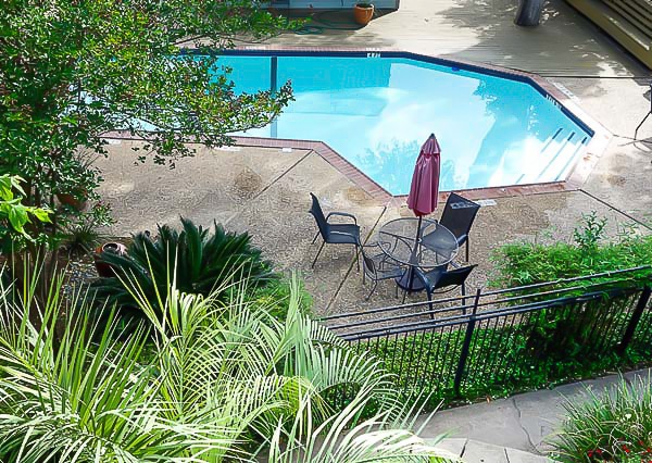 Fenced swimming pool with patio table, chairs, umbrella, and surrounding landscaping.