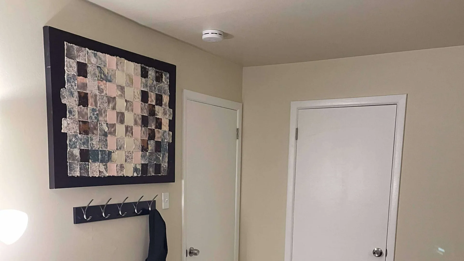 Entry hall with a patchwork wall hanging, a row of coat hooks, and two white doors.