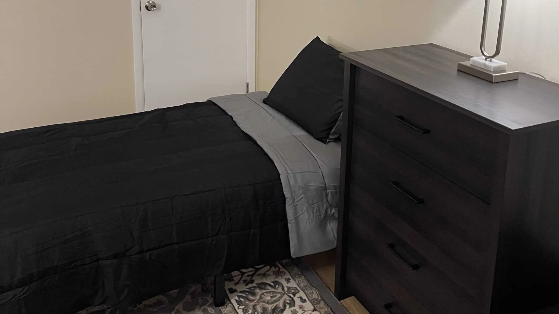 Bed in black and gray bedding next to a dark dresser in a corner bedroom.