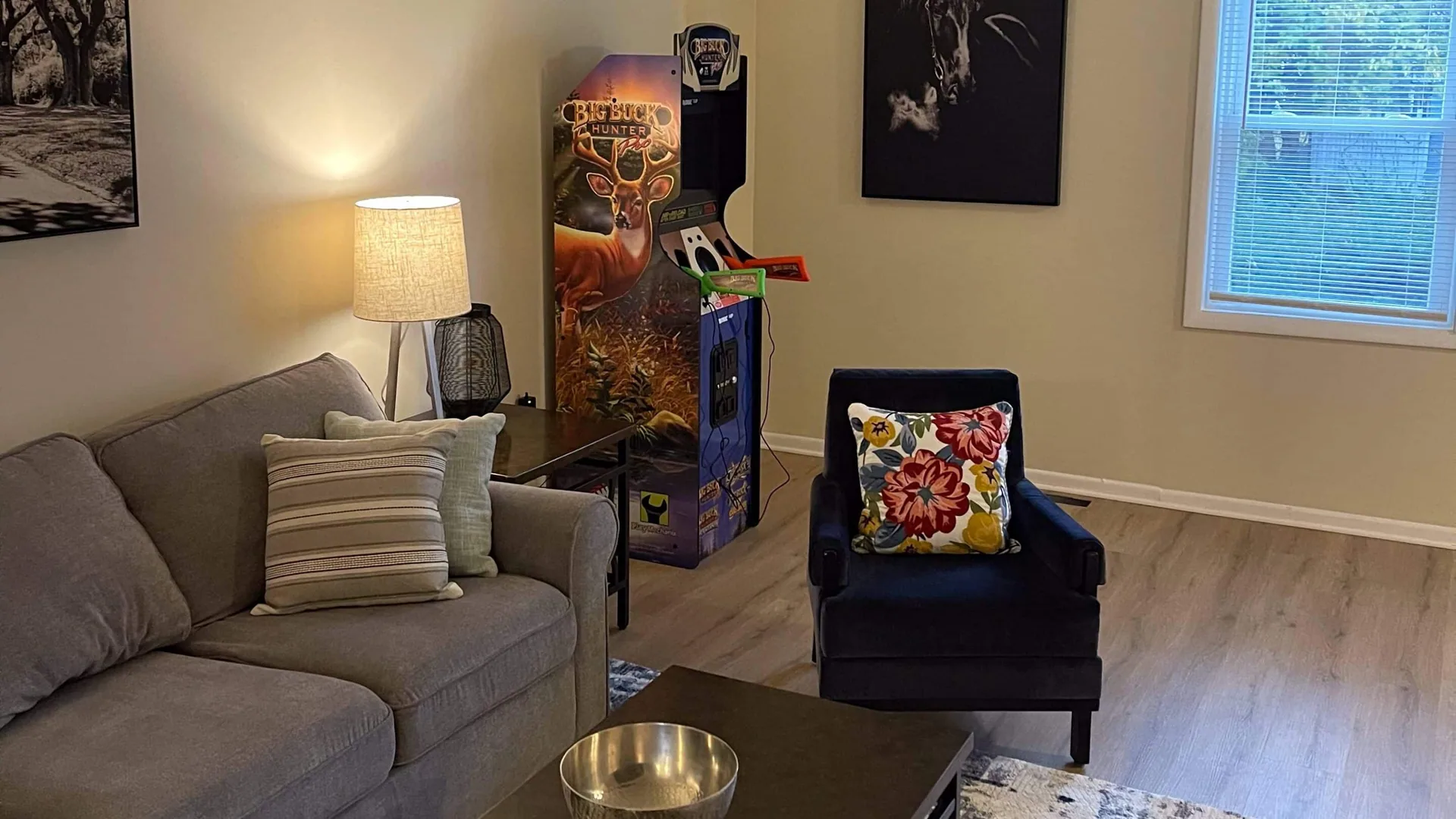 Resident living room: a gray sectional with cushions, a floor lamp, a navy armchair, and an arcade cabinet against the far wall.