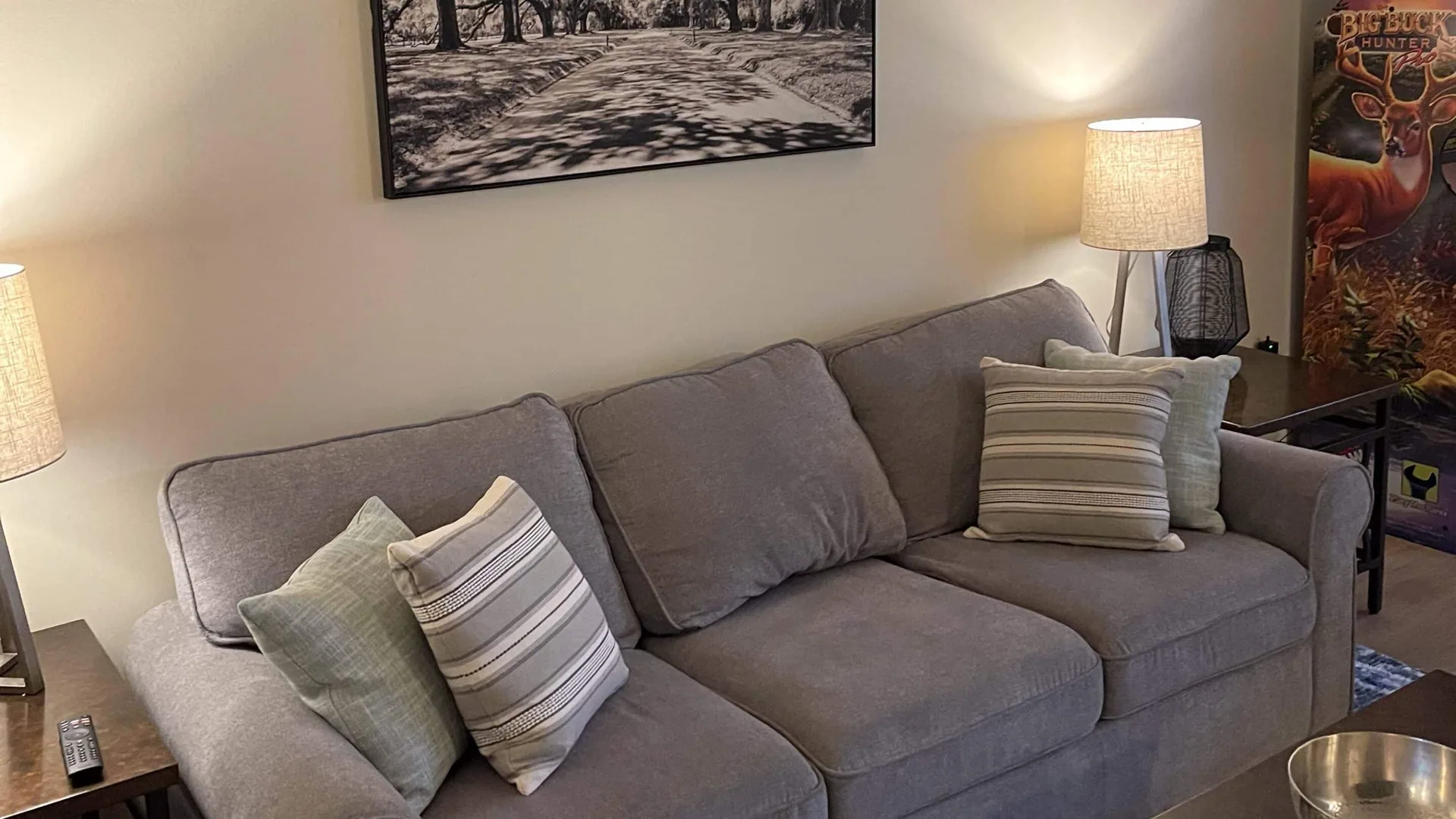 Grey sofa with striped cushions beneath framed artwork, lit by a table lamp.