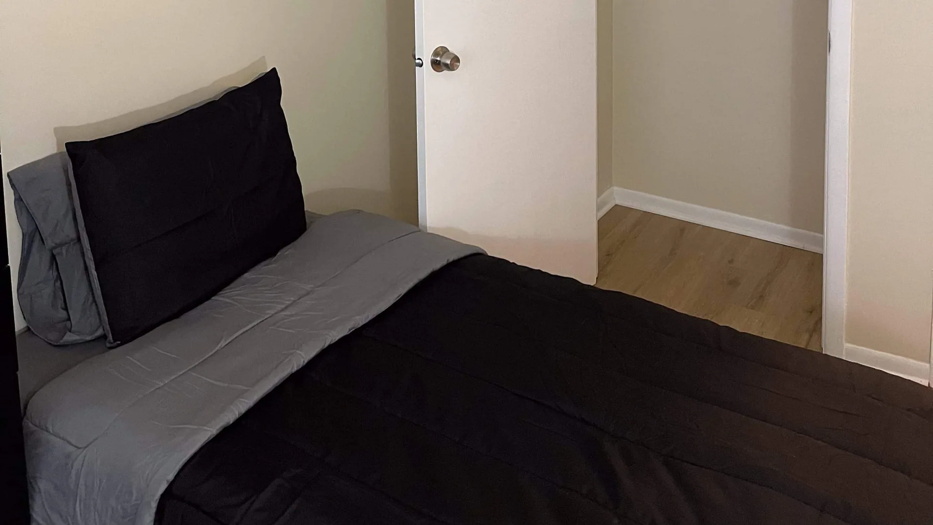 Single bed in gray and black bedding beside a white door.