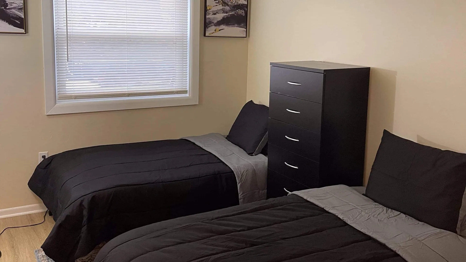 Twin bed beside a tall dark dresser, below a window with blinds.