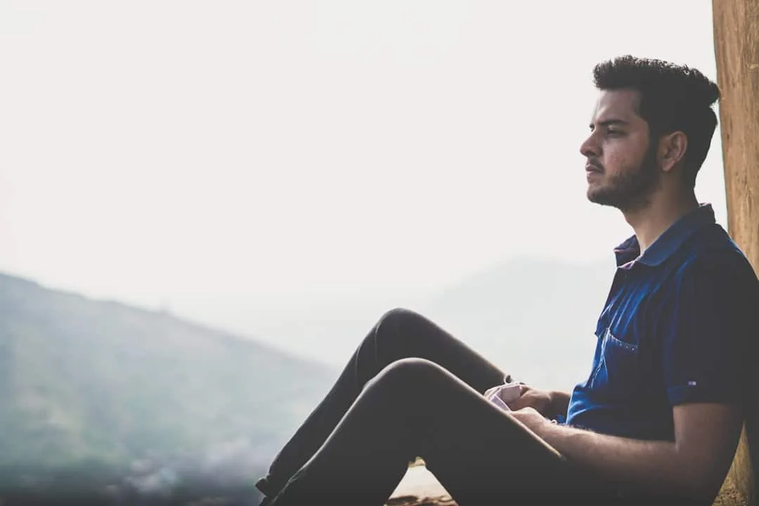 a man sitting on a ledge with a mountain in the background -- Photo by Harsh Gupta on Unsplash