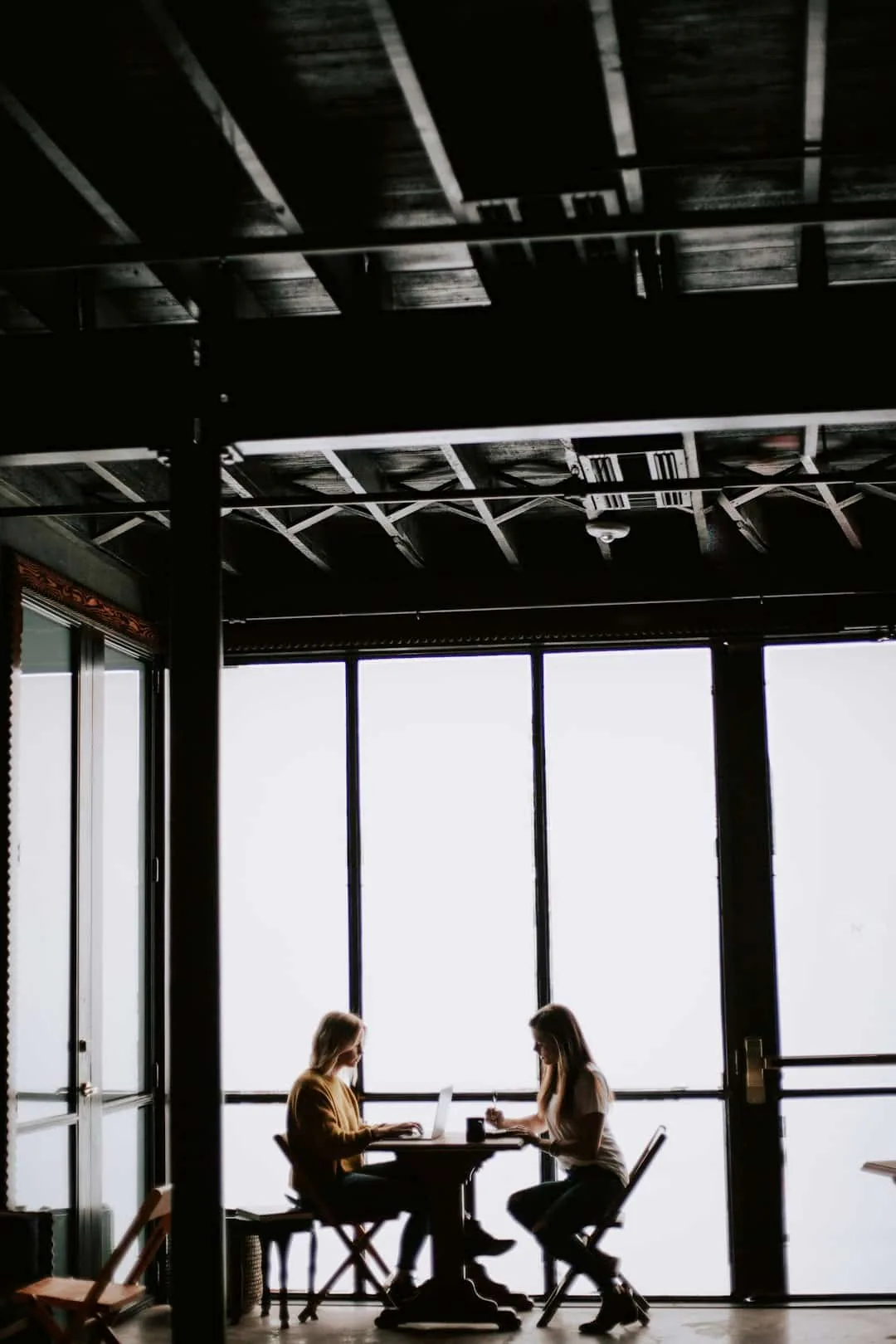 photo of two women facing each other sitting in front of table near glass wall -- Photo by Christin Hume on Unsplash