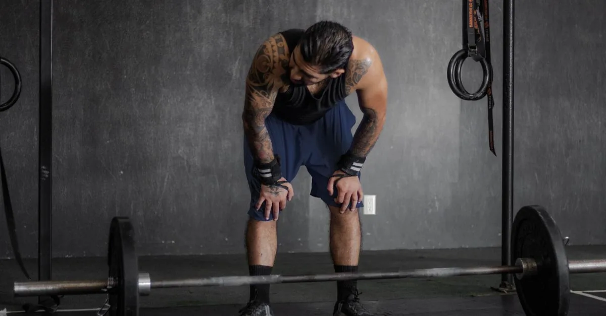 A muscular man with tattoos rests after an intense weightlifting session in the gym.