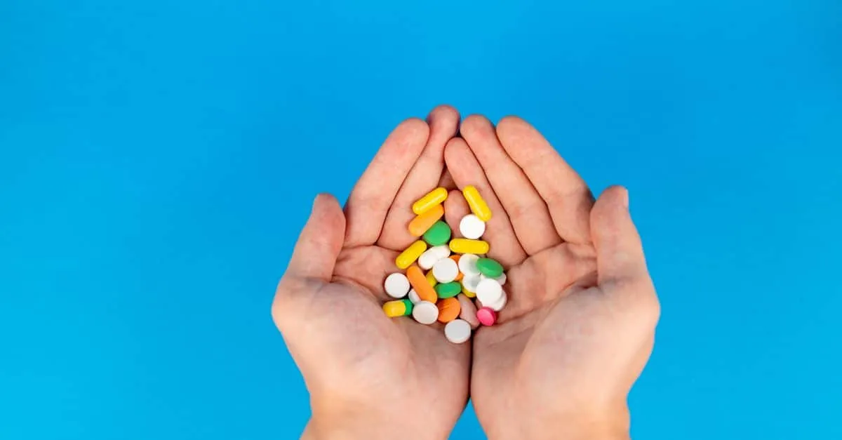 A pair of hands gently cradles a variety of colorful pills against a vibrant blue backdrop, symbolizing healthcare.