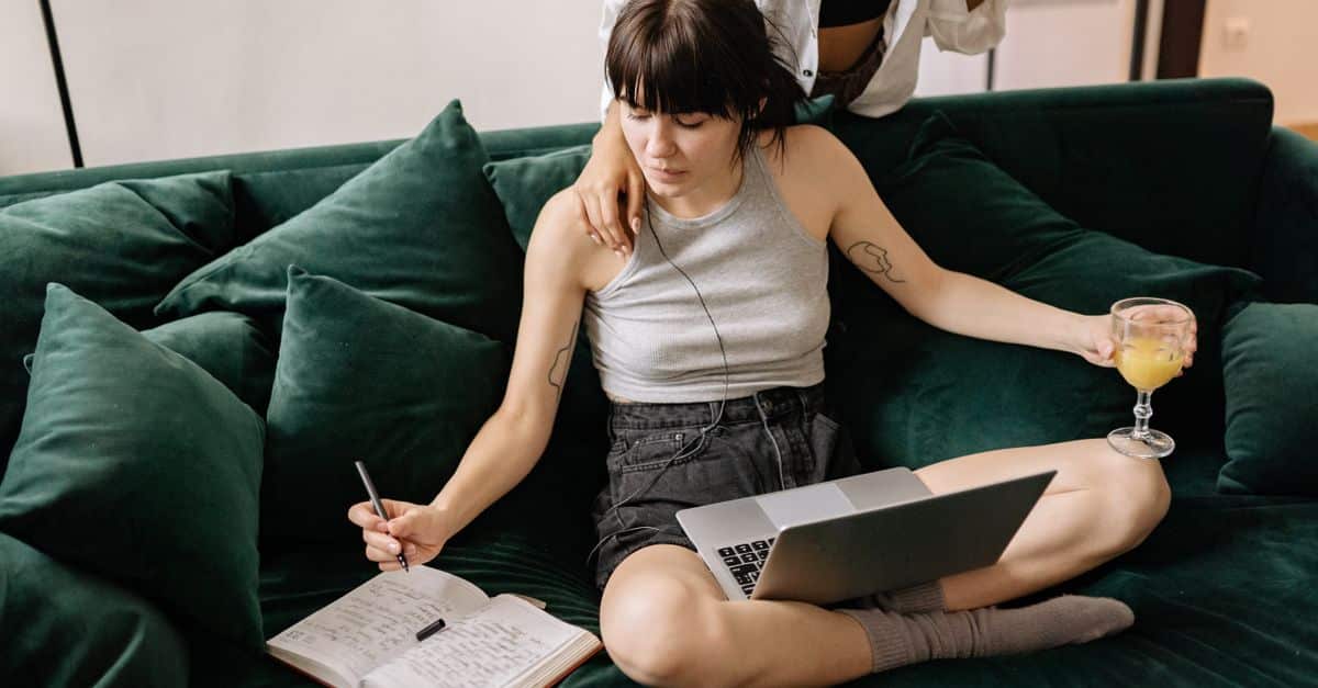 Couple relaxing on a sofa while working from home, enjoying drinks and writing notes in a notebook.