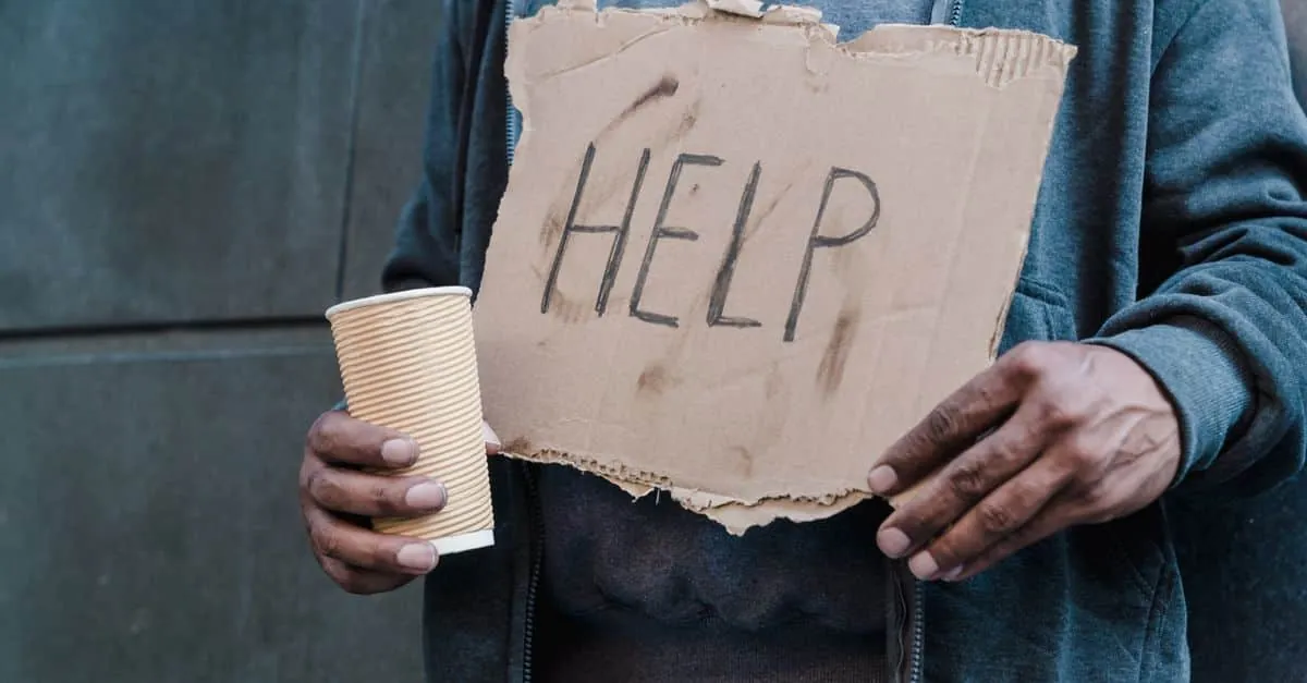 Close-up of a person holding a cardboard sign with 'Help' and a paper cup, representing need and assistance.