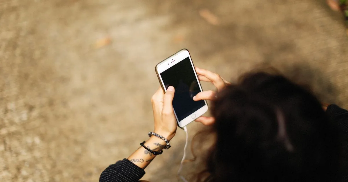 High-angle view of a young woman holding a smartphone outdoors, focusing on her hands and device.