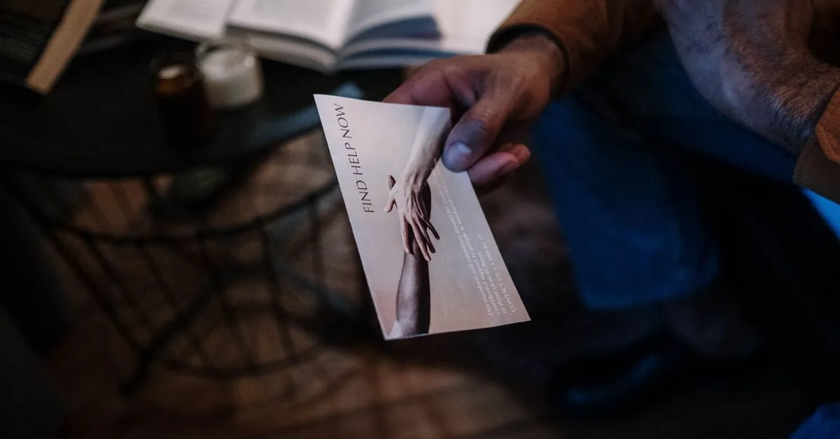 A person holds a help brochure in a cozy indoor setting, symbolizing support and mental health awareness.