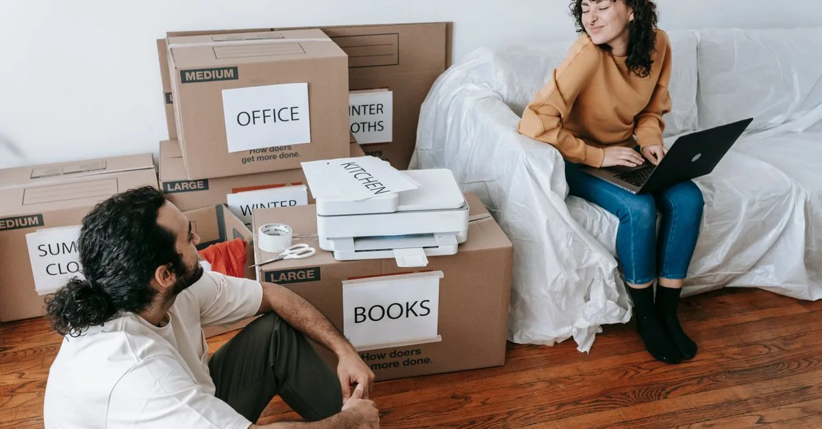 Young couple organizing boxes and relaxing with laptop during moving day indoors.