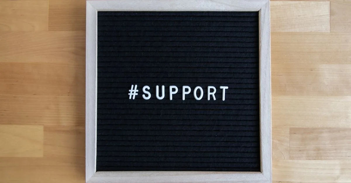 Black letter board displaying the word '#support' on a wooden table surface.