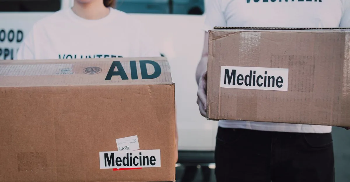 Volunteers holding boxes labeled 'AID' and 'Medicine', preparing donations.