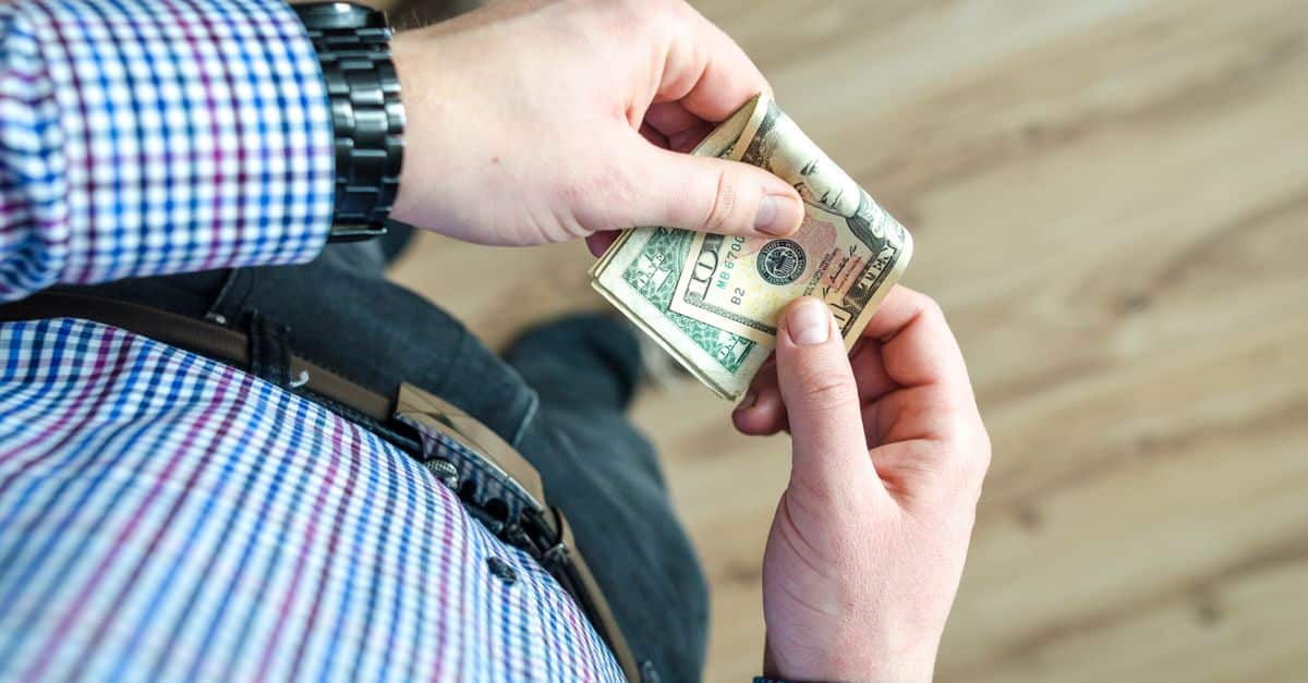 Close-up view of a man in casual clothes holding US dollar bills in his hands.