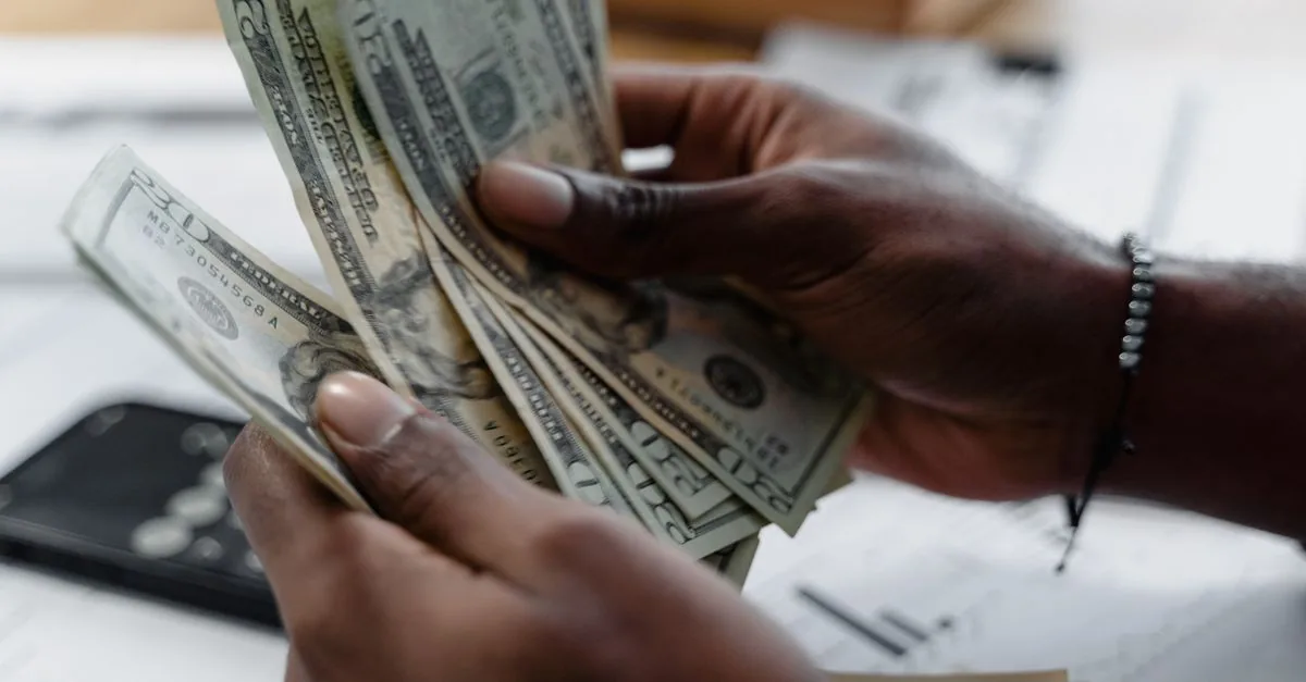 Detailed image of hands counting US dollar bills on a desk, emphasizing finance and budgeting.