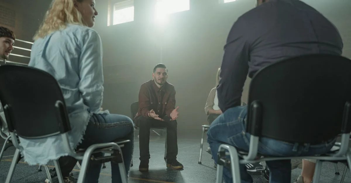 A diverse group of adults in a supportive discussion setting indoors with sunrays.