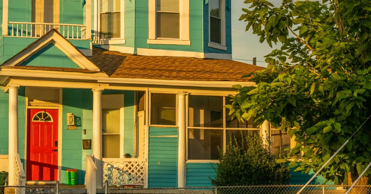 A picturesque turquoise house with a red door illuminated by sunset in Newport News, Virginia.