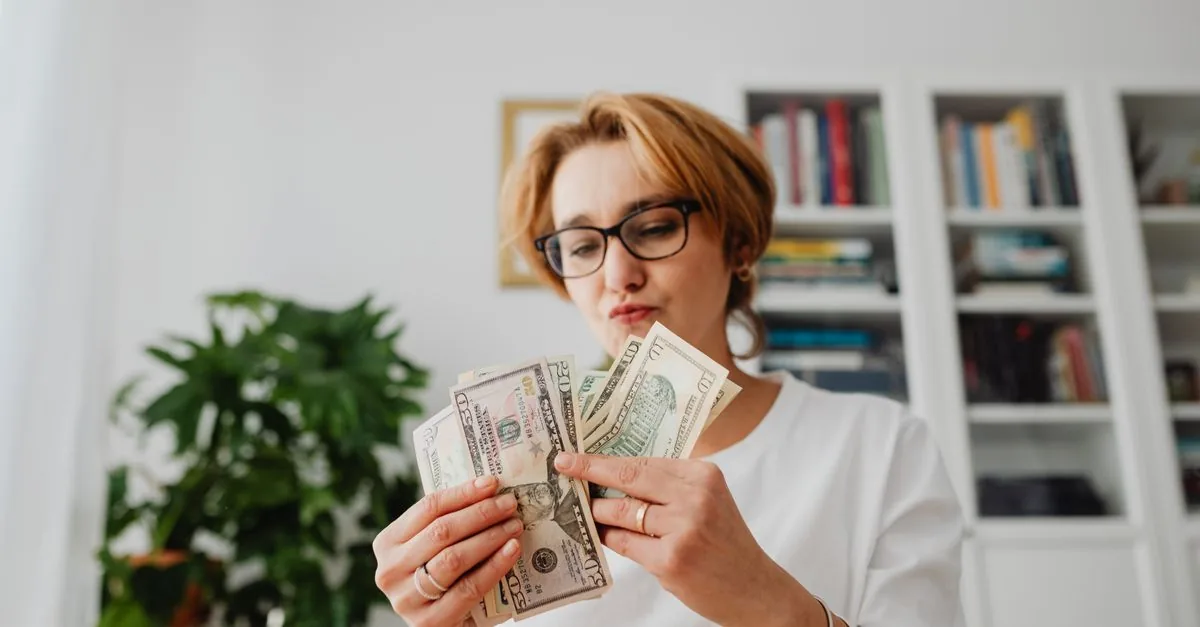 Woman with eyeglasses counting dollar bills in a home setting
