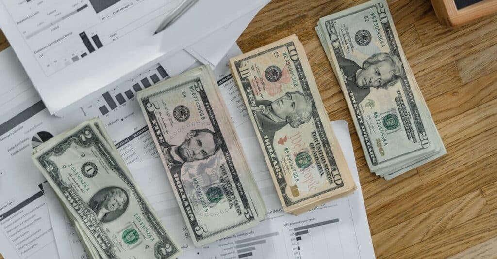 Stacks of US Dollar banknotes placed over financial documents and reports on a desk.