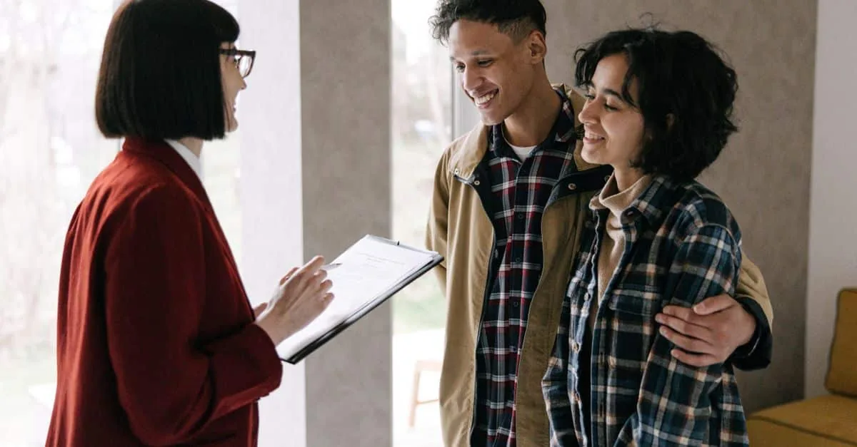 A young couple discusses housing options with a real estate agent inside a modern apartment.