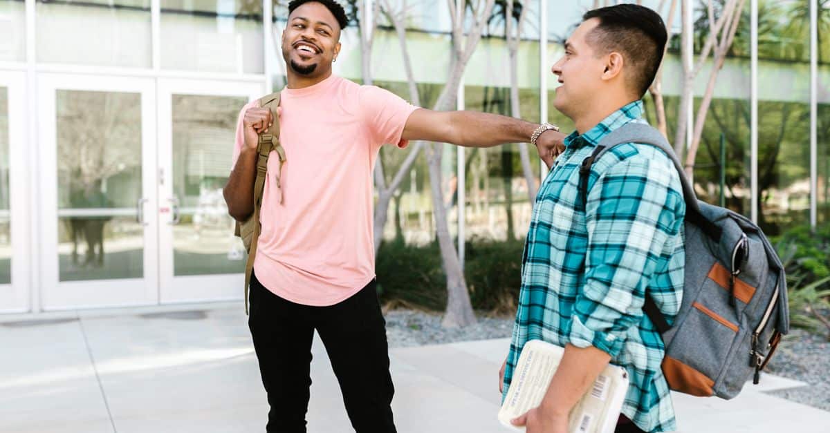 Two college students enjoying a friendly conversation on campus, carrying backpacks.