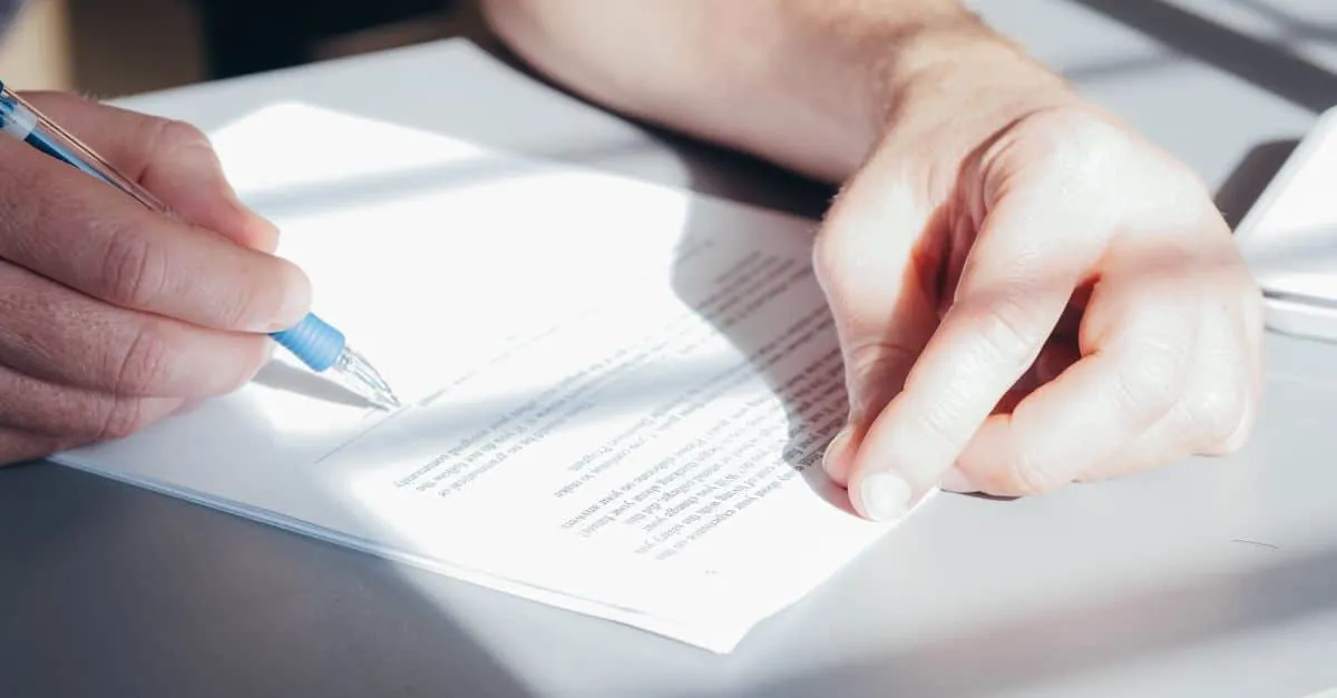 Hands signing a contract with a blue pen, close-up view.
