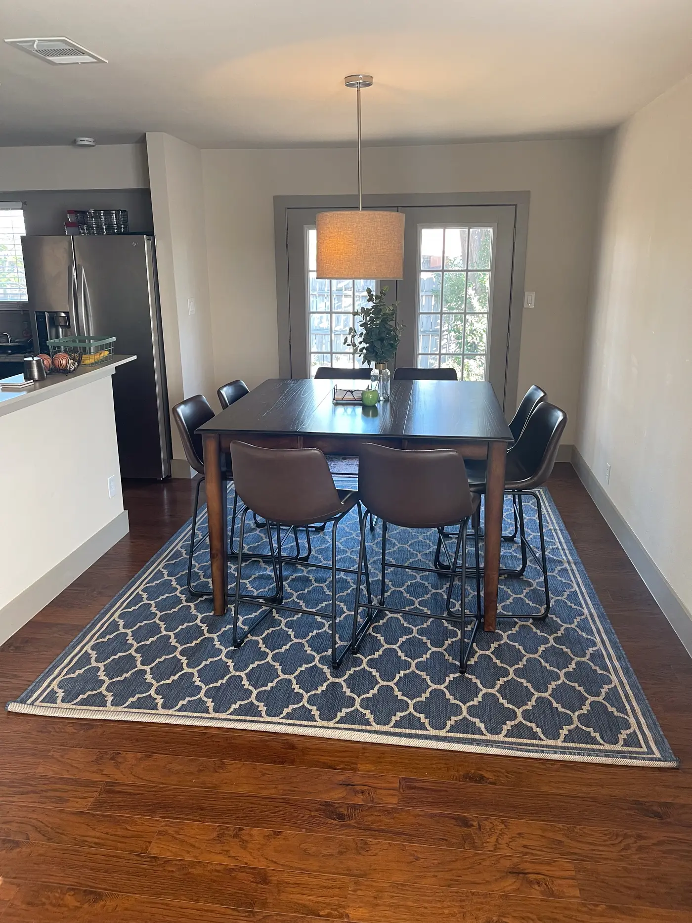 Dining table and chairs on a patterned rug with the kitchen beyond.