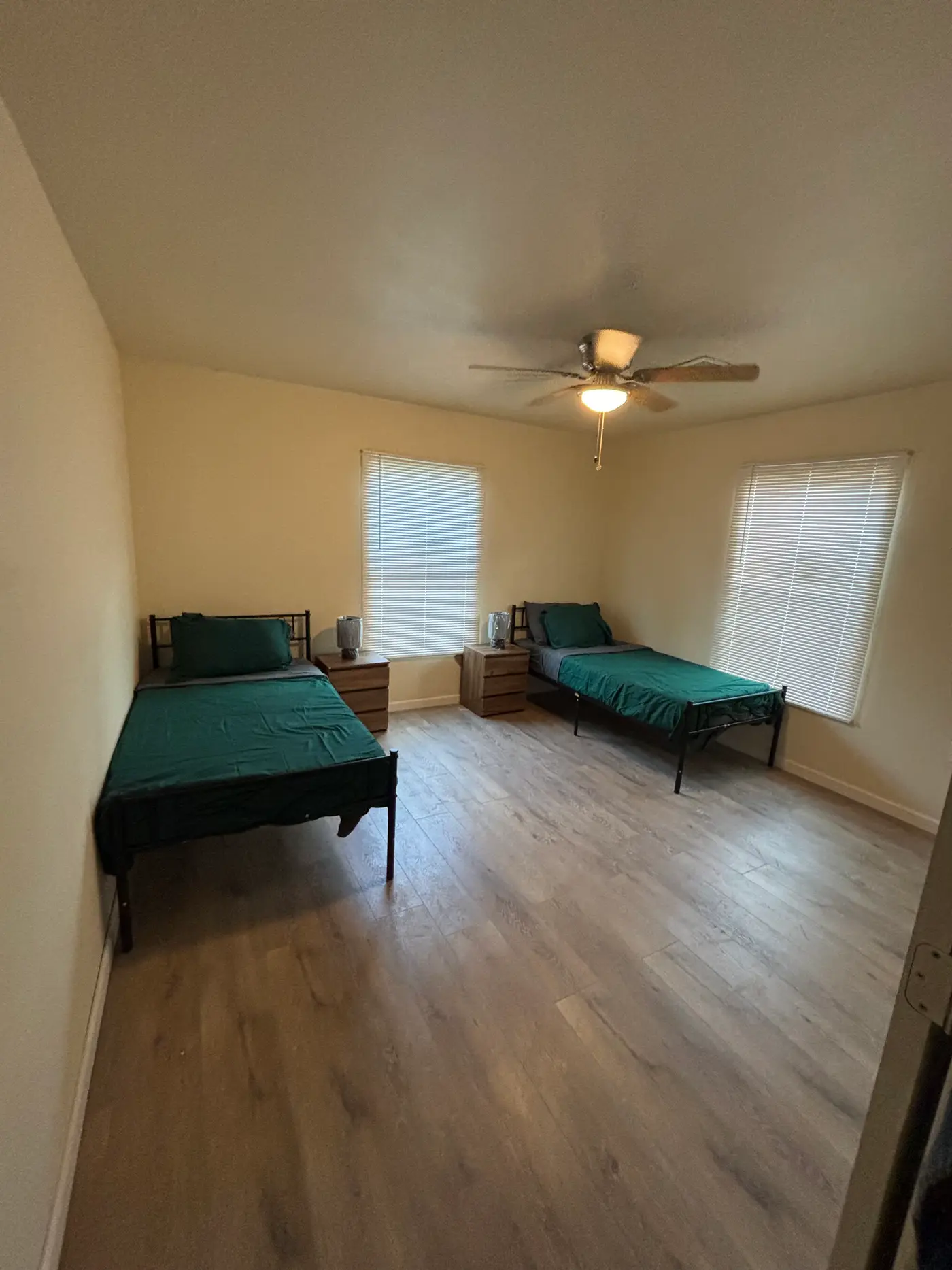 Bedroom with two single beds in green bedding beneath shuttered windows.