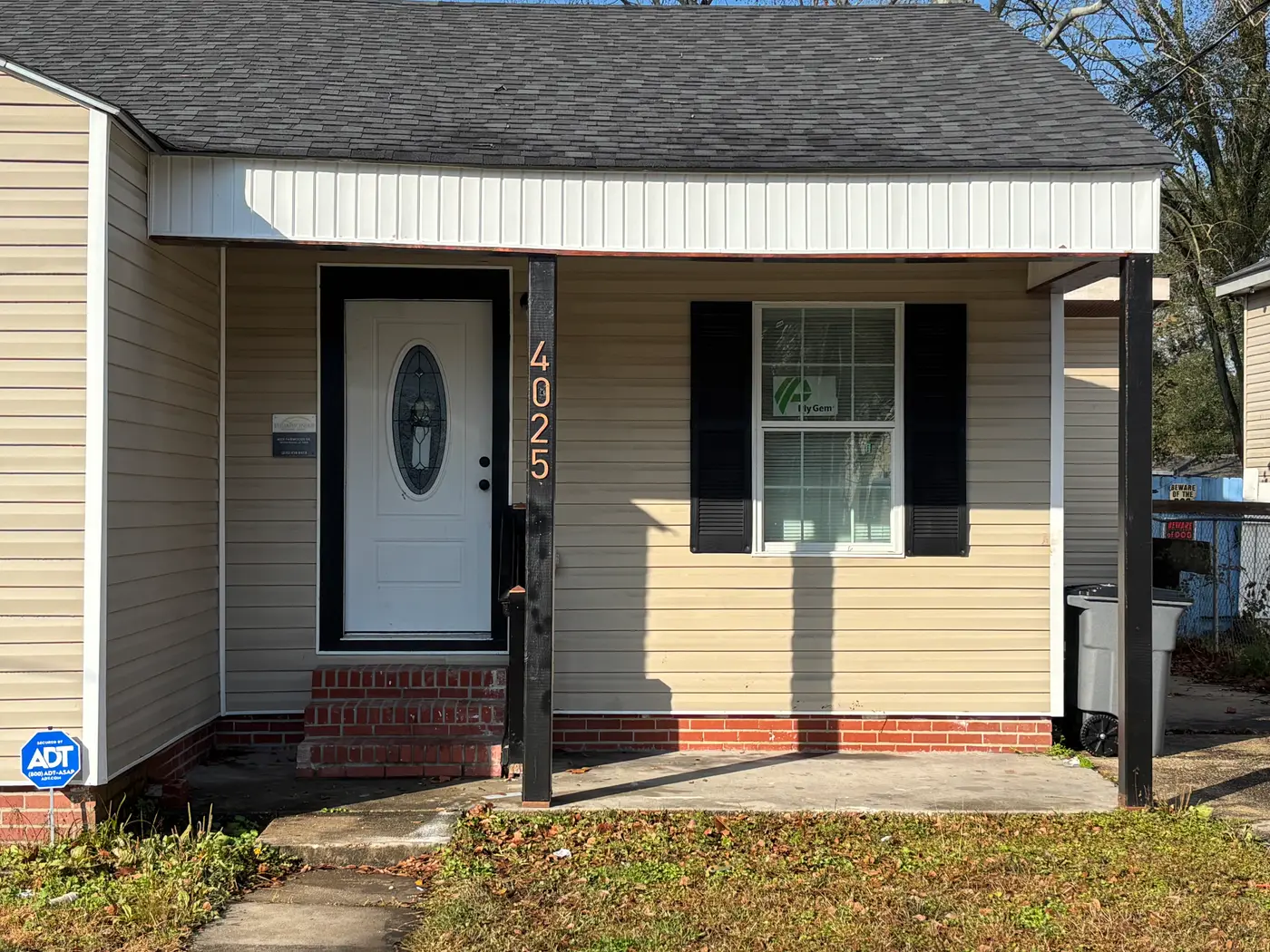 Front of the cream weatherboard cottage with black shutters and a brick step.