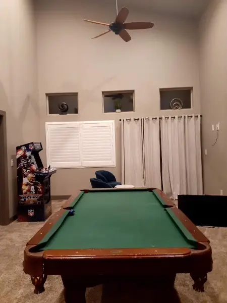Pool table with a cue rack and a curtained window.