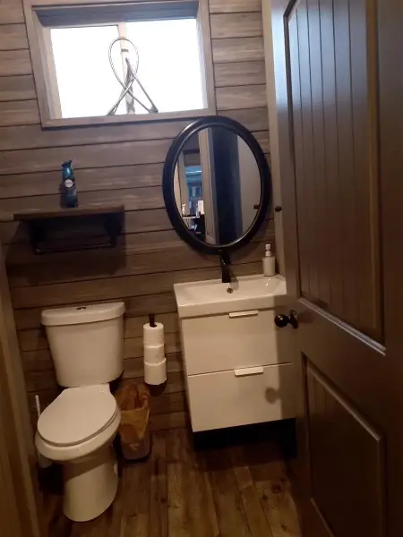 Bathroom with a vanity, oval mirror and paneled wall.