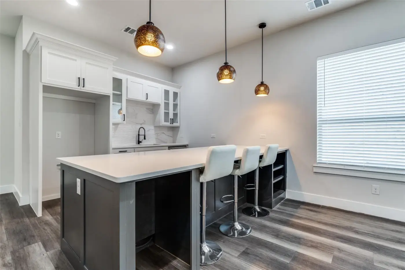 Kitchen island with white bar stools under pendant lights.