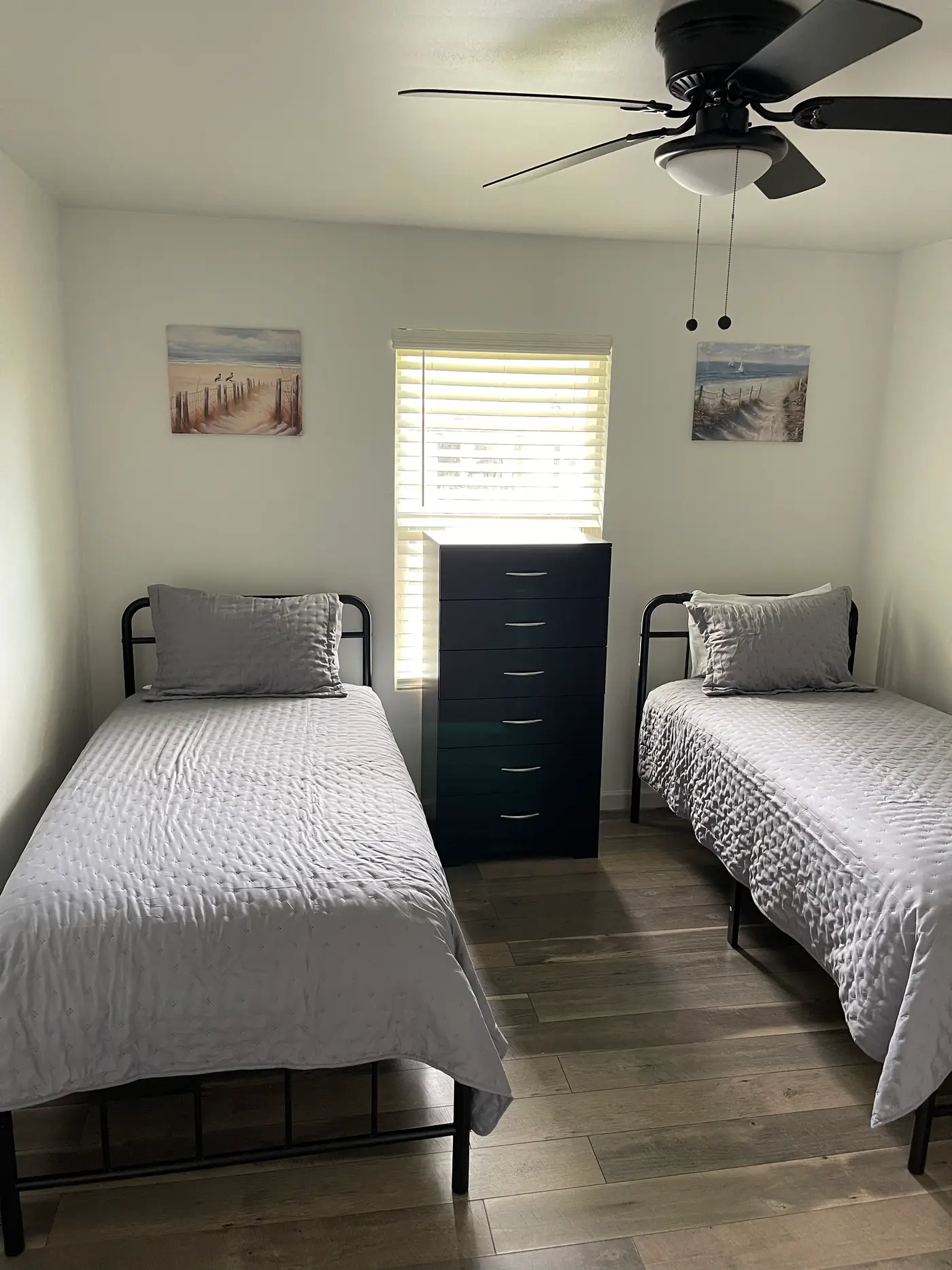 Bedroom with two single beds in gray bedding either side of a dark dresser.