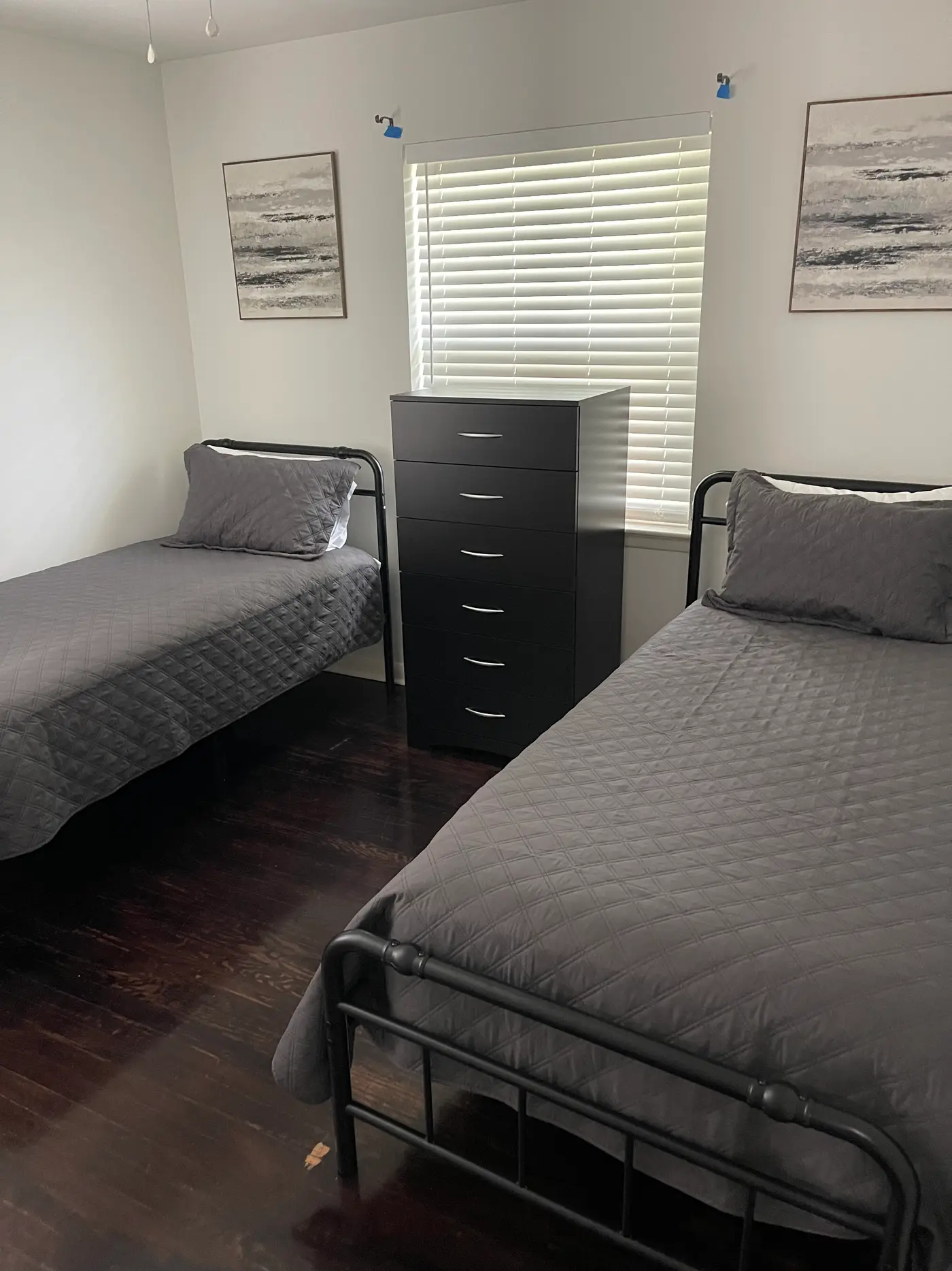 Bedroom with two single beds in gray bedding beneath a shuttered window.