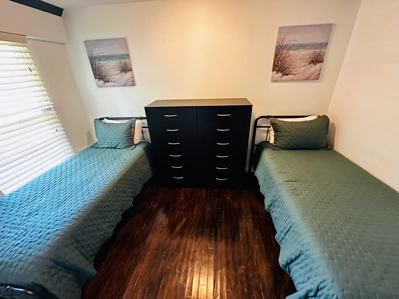 Bedroom with two single beds in black bedding either side of a dresser.
