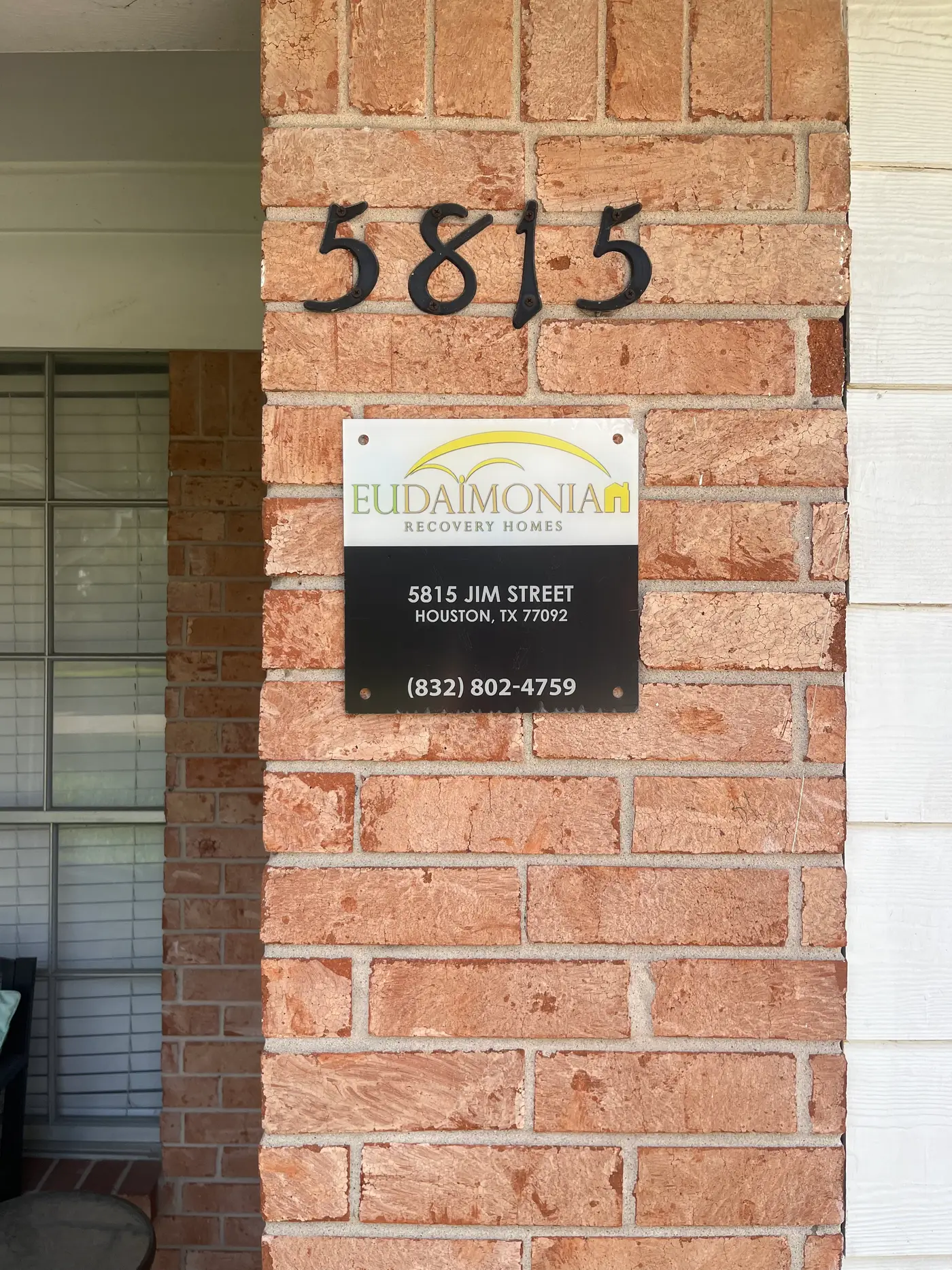 Eudaimonia Recovery Homes sign mounted on the brick beside the front door.