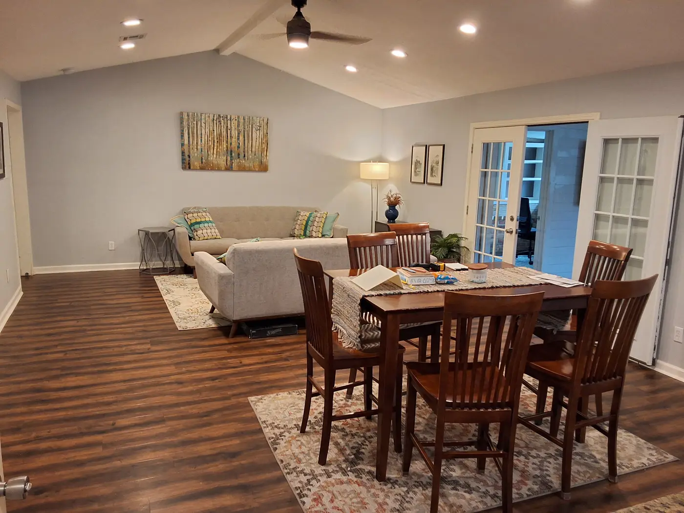 Dining table and chairs with the living room beyond, on dark wood flooring.