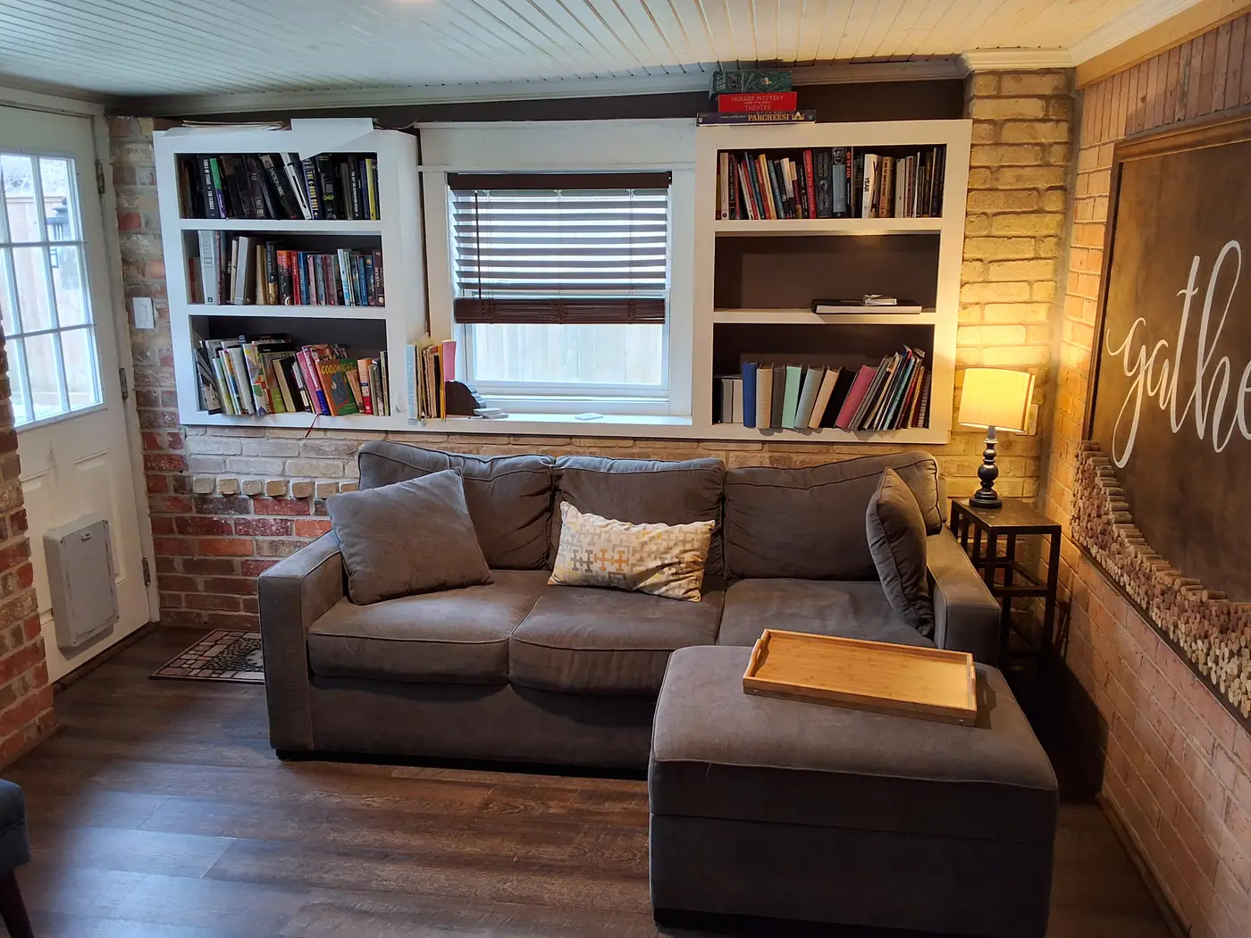 Den with built-in bookshelves, a gray sofa and a brick wall.