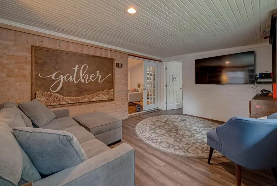 Living room with a gray sectional beneath a large “gather” sign.