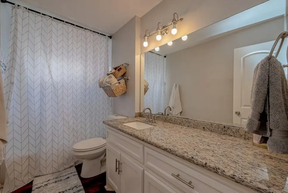 Bathroom vanity with a granite top and a lit mirror.