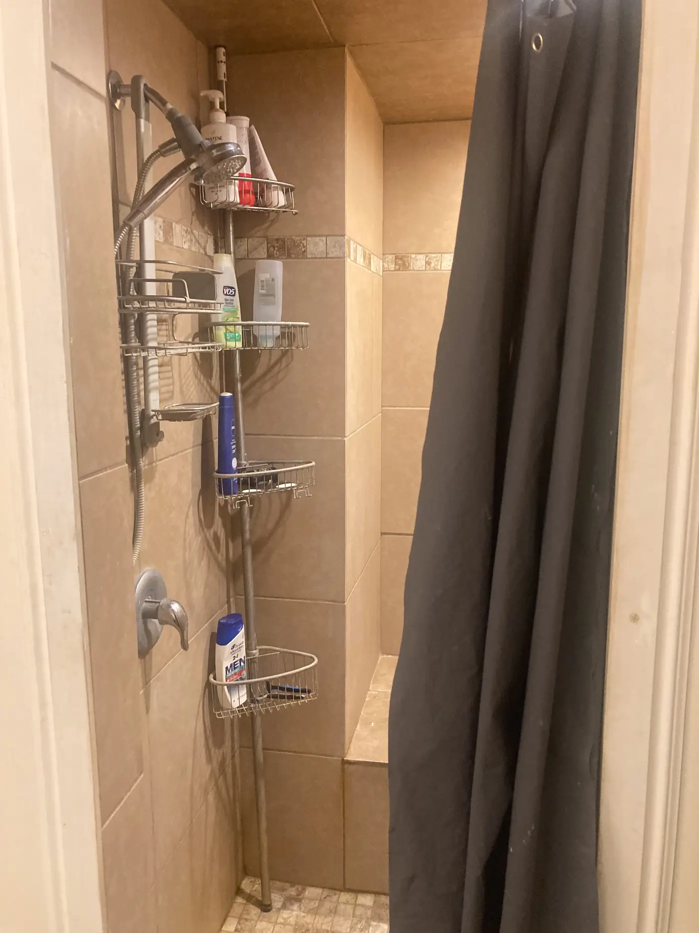Shower with a curtain, corner caddy and tiled surround.